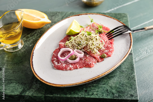 Plate with tasty veal carpaccio, lemon and oil on color wooden background