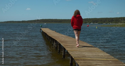 Young white woman walking on a wooden bridge over a lake. View from behind photo