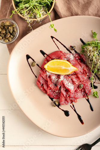 Plate with tasty veal carpaccio on light wooden background, closeup