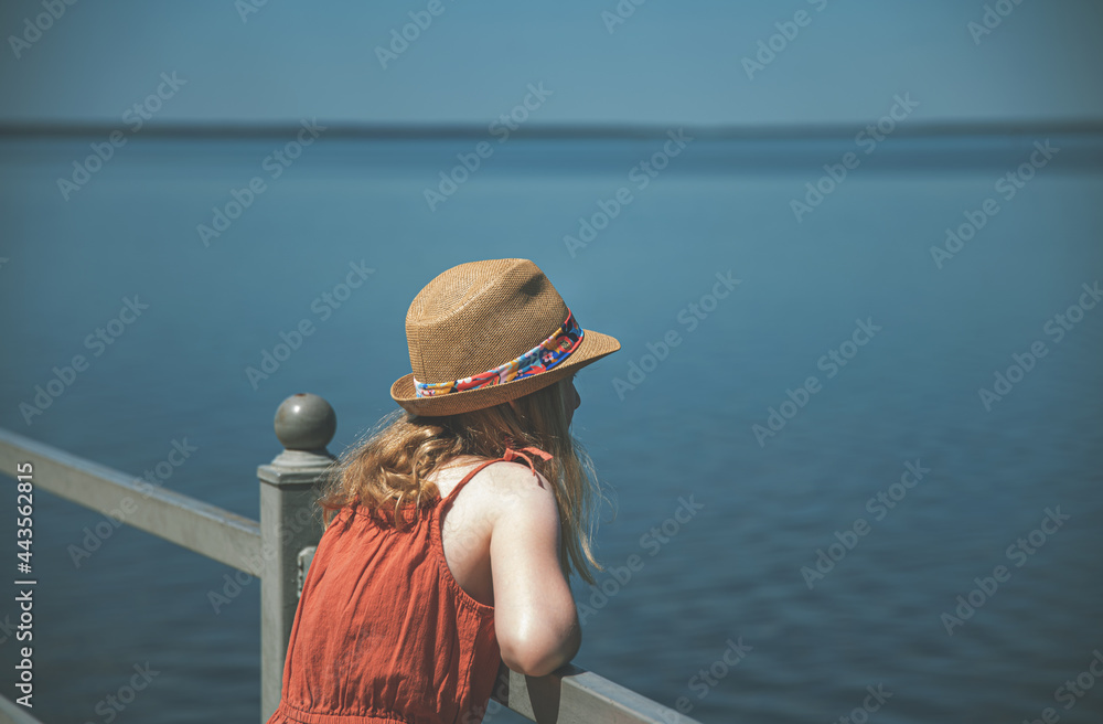 a girl stands on the seafront  and looks dreamily into the distance on a sunny summer day, without face