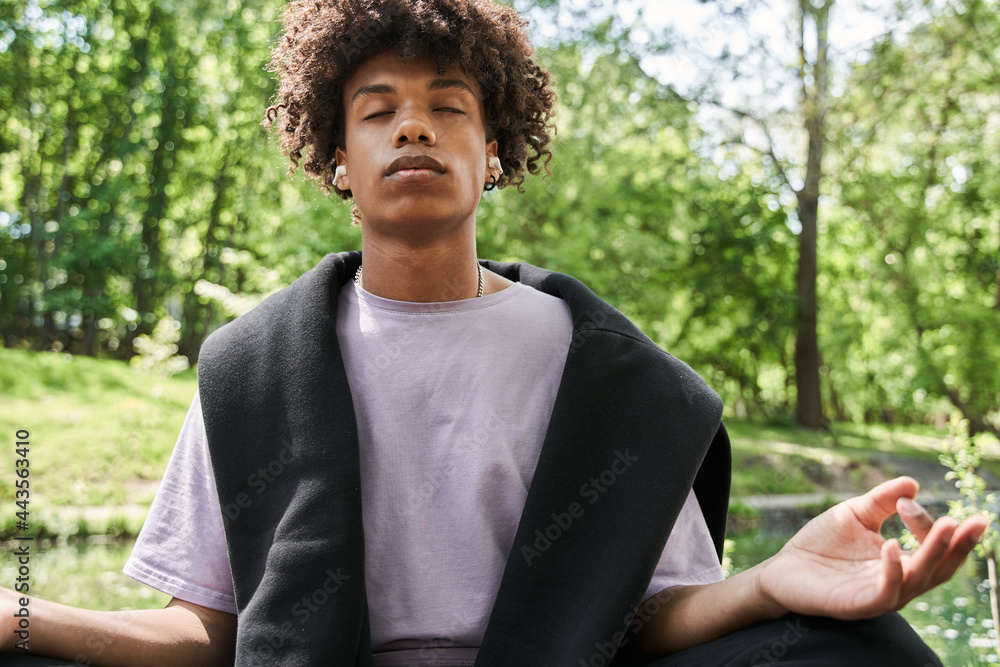 Fototapeta premium Man keeping eyes closed and meditating at the cozy forest or park