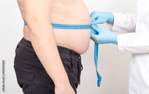 Foto Doctor nutritionist measures the big fat belly of a male patient with a measuring tape