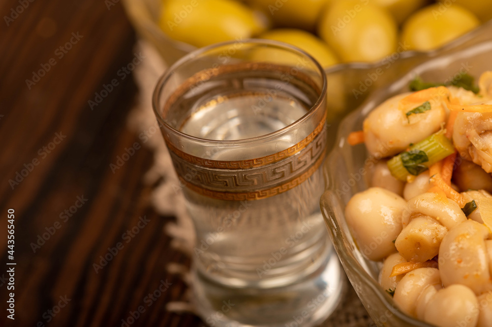 A glass of vodka and salted mushrooms and salted olives in glass dishes on a background of homespun fabric with a rough texture. Close-up Selective focus. A glass of vodka and salted mushrooms and salted olives in glass dishes on a background of homespun fabric with a rough texture. Close-up Selective focus.