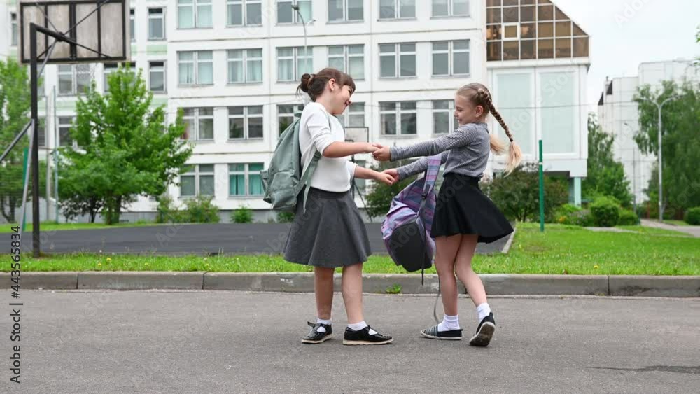 two cute happy girls schoolgirls with backpacks are playing near the school. High quality two cute happy girls schoolgirls with backpacks are playing near the school. High quality