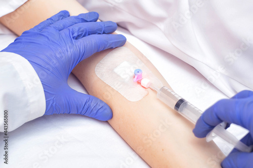 The doctor injects the medicine from a syringe into the female patient's venous catheter. Pain reliever and anti-inflammatory agent, vasodilator photo