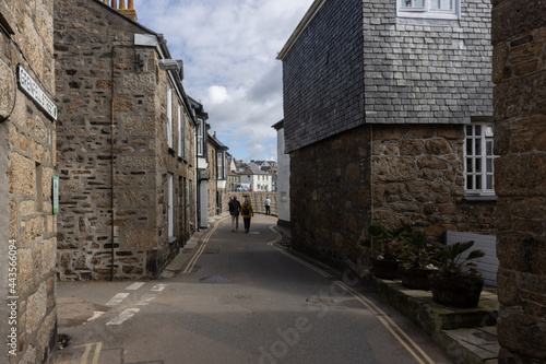 A couple walk hand in hand through a narrow street of granite cottages in traditional fishing village of Mousehole, Cornwall