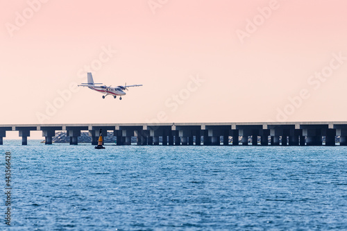A light twin-engine propeller plane lands on a runway built in the sea. Concept of tourist excursions and civil aviation in the resort