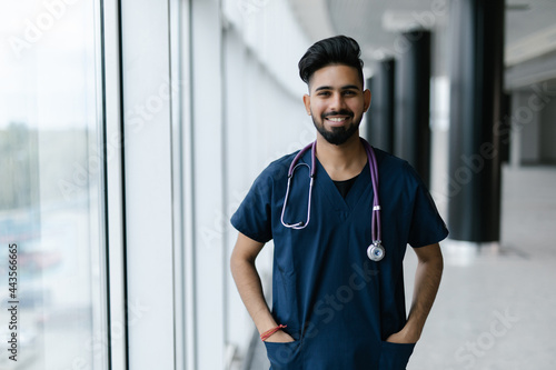 Portrait of a smiling Indian male medical doctor walking inside hospital.