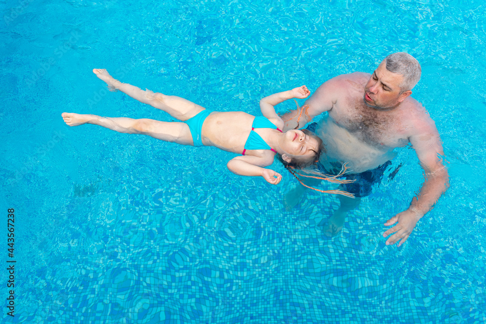 dad teaches his little daughter to float on the water. family in the swimming pool