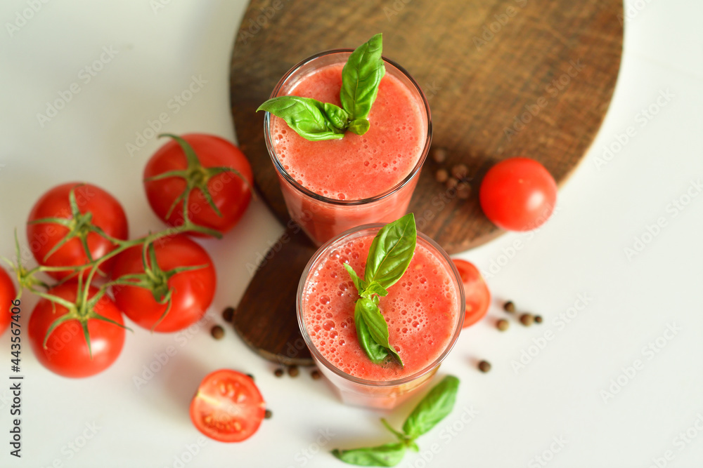 Two glasses of fresh organic tomato juice decorated with raw tomatoes and green leaves of basil on light background.Healthy diet nutrition concept. Two glasses of fresh organic tomato juice decorated with raw tomatoes and green leaves of basil on light background.Healthy diet nutrition concept.