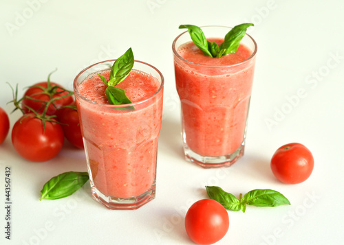 Two glasses of fresh organic tomato juice decorated with raw tomatoes and green leaves of basil on light background.Healthy diet nutrition concept.