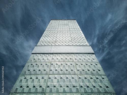 Bottom-up view of a high concrete wall with a decorative embossed pattern on a cloudless day.