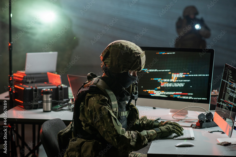 Gloved cyber criminal in camouflage attire decoding or stealing information