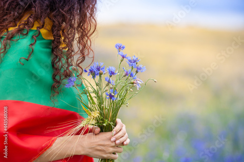 Woman covered with flag of Lithuania holding bouquet of blue cornflowers in a rye field. Lithuanian Flag Day. Independence restoration Day. King mindaugas day. photo