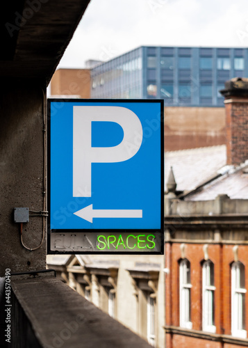 Multi storey car park P sign blue with bright green neon writing showing spaces and arrow. Carpark spaces available empty in England UK. Electric sign board.