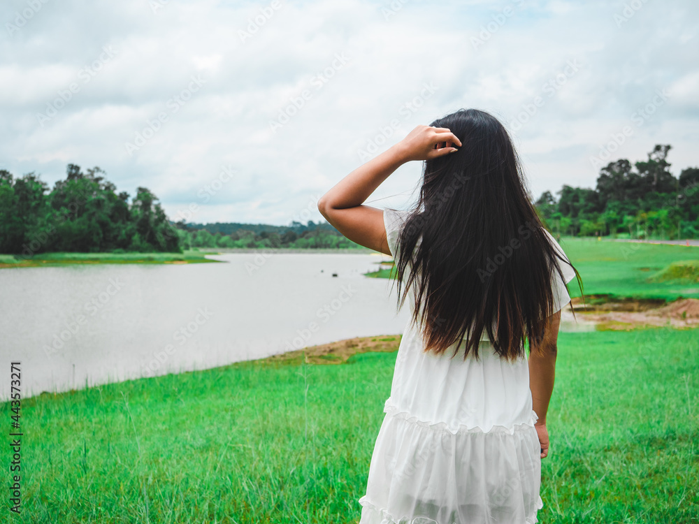 Asian girl stand with river and forest and mountain fresh nature in vacation,Long hair,Backside Woman white dress in green grass filed and lake tree cloudy of sky landscape background Asian girl stand with river and forest and mountain fresh nature in vacation,Long hair,Backside Woman white dress in green grass filed and lake tree cloudy of sky landscape background