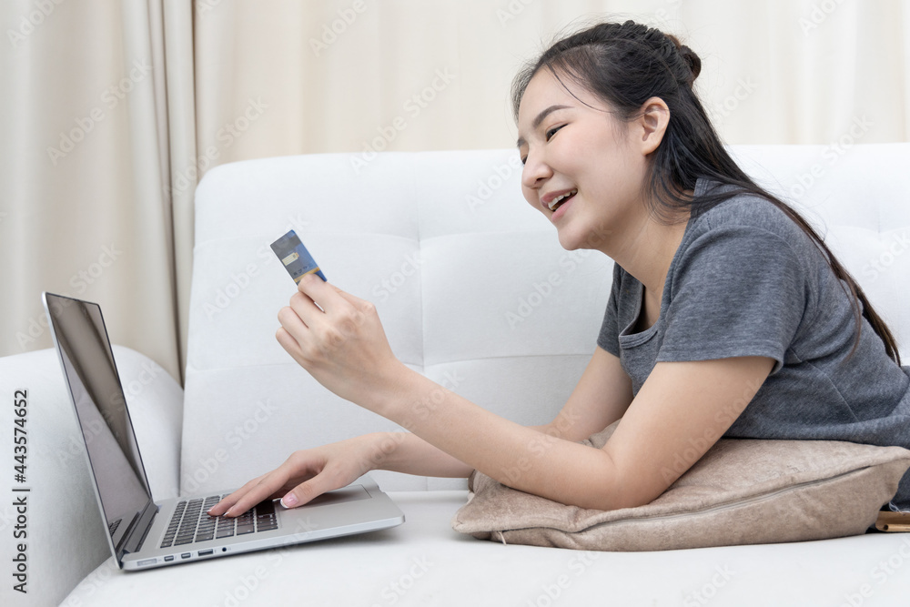 Asian woman lounging on sofa and using laptop to shop online with credit card to register for payment or online transactions, Financial transactions and Internet security, Shopping with credit card. Asian woman lounging on sofa and using laptop to shop online with credit card to register for payment or online transactions, Financial transactions and Internet security, Shopping with credit card.