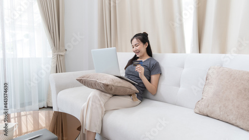 Asian woman sitting on sofa and using laptop to shop online with credit card to register for payment or online transactions, Financial transactions and Internet security, Shopping with credit card.