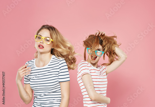two girls standing side by side in striped t-shirts friendship pink background fashion