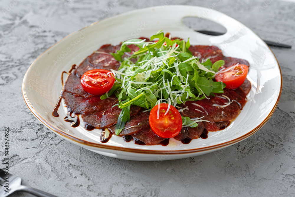 Beef carpaccio with arugula and parmesan on gray surface Beef carpaccio with arugula and parmesan on gray surface