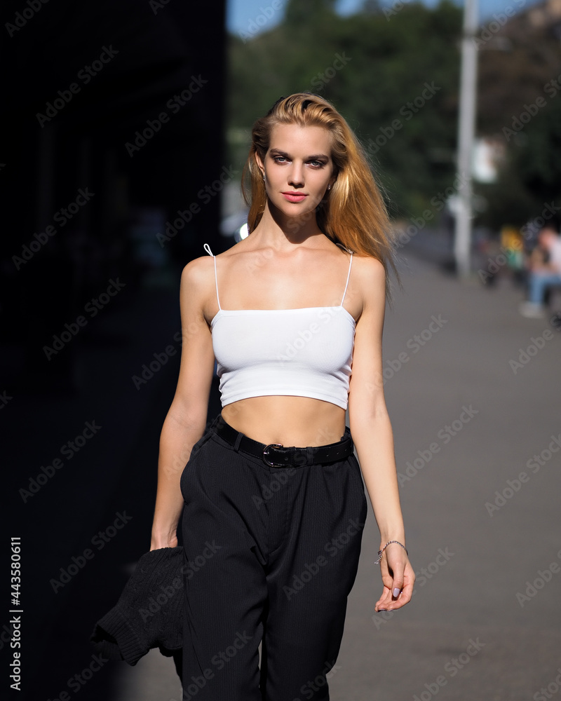Fototapeta premium Blonde outdoors in white top, black pants and heels
