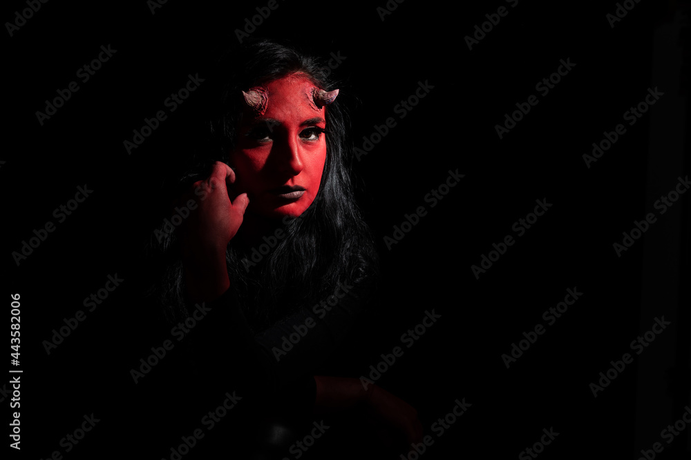 Portrait of sexy woman with long black hair and with face paint for halloween, demon woman with red face and small horns on black background. Halloween concept. Halloween Makeup Portrait of sexy woman with long black hair and with face paint for halloween, demon woman with red face and small horns on black background. Halloween concept. Halloween Makeup