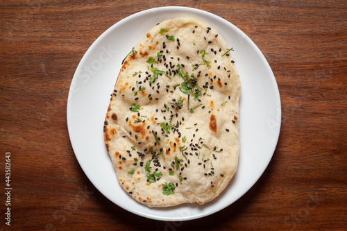 Close-up of fresh, hot two tandoori roti or naan garnished with black till and green fresh coriander leaves. A typical, traditional north indian panjabi food. in a white plate. photo