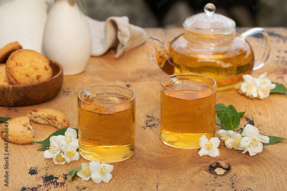 Green Chinese tea with jasmine in mugs and a teapot on a wooden table top with a jasmine flowers. Green Chinese tea with jasmine in mugs and a teapot on a wooden table top with a jasmine flowers.