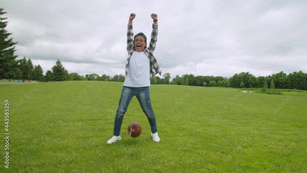 Cheerful cute school age african boy running on field, crossing goal line with ball and celebrating touchdown with winning gesture, expressing happiness and excitement during american football game. Cheerful cute school age african boy running on field, crossing goal line with ball and celebrating touchdown with winning gesture, expressing happiness and excitement during american football game.