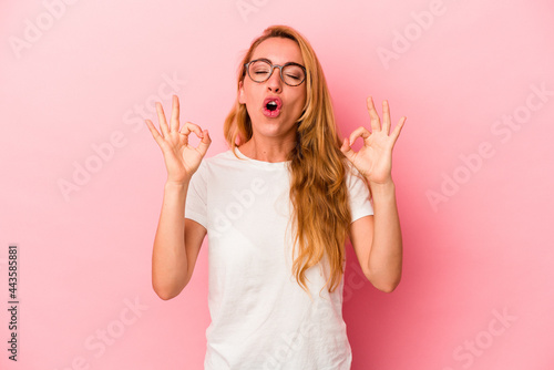 Caucasian blonde woman isolated on pink background relaxes after hard working day, she is performing yoga.