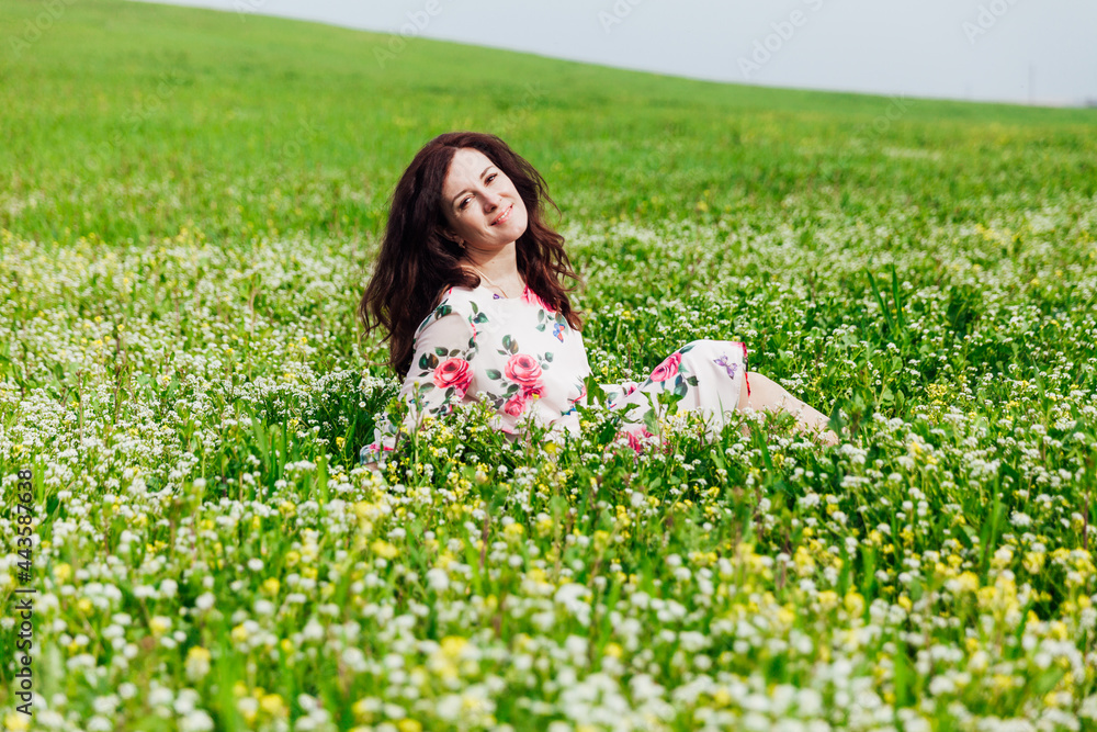 Beautiful brunette woman in dress with flowers sits in spring field Beautiful brunette woman in dress with flowers sits in spring field