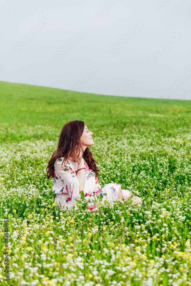 Beautiful brunette woman in dress with flowers sits in spring field Beautiful brunette woman in dress with flowers sits in spring field