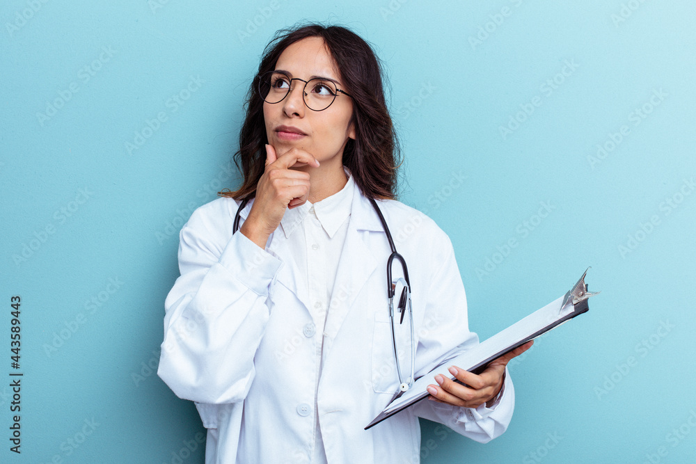 Young doctor mexican woman isolated on blue background looking sideways with doubtful and skeptical expression. Young doctor mexican woman isolated on blue background looking sideways with doubtful and skeptical expression.