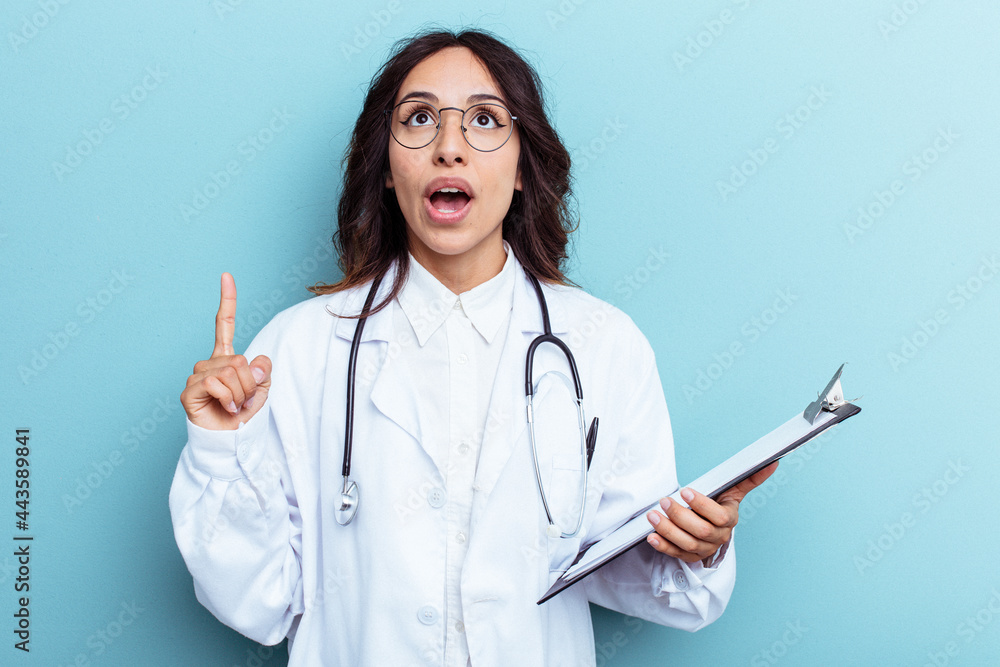 Young doctor mexican woman isolated on blue background pointing upside with opened mouth. Young doctor mexican woman isolated on blue background pointing upside with opened mouth.