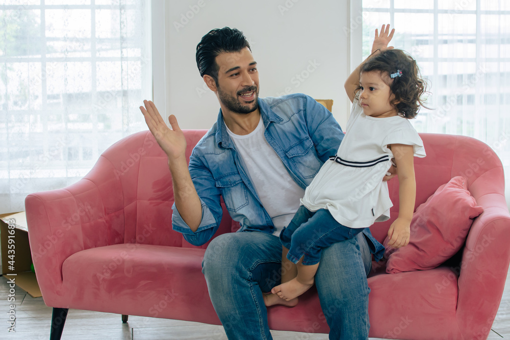 Happy handsome beard Caucasian father and little cute girl playing together with fun, smiling with love and happiness, giving high five while sitting on pink couch at comfortable home or house. Happy handsome beard Caucasian father and little cute girl playing together with fun, smiling with love and happiness, giving high five while sitting on pink couch at comfortable home or house.