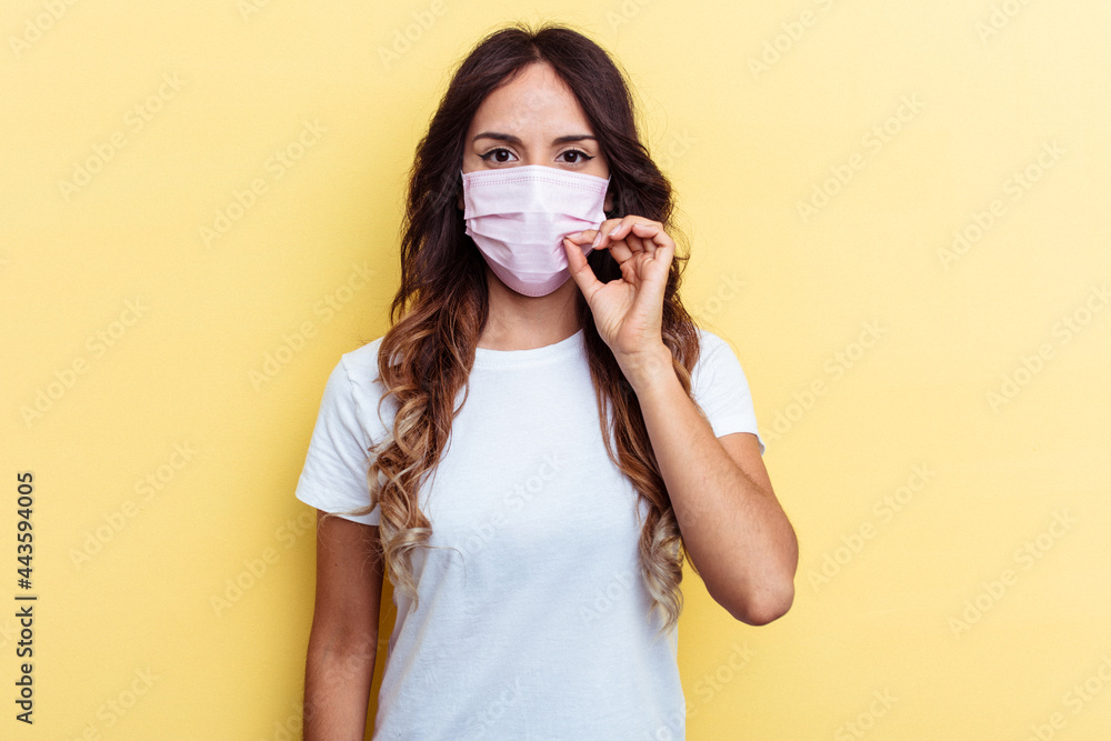 Young mixed race woman wearing a protection for virus isolated on yellow background with fingers on lips keeping a secret. Young mixed race woman wearing a protection for virus isolated on yellow background with fingers on lips keeping a secret.