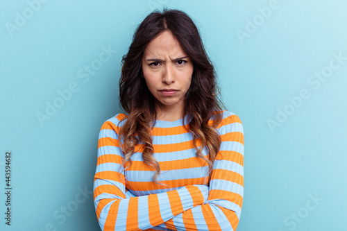Young mexican woman isolated on blue background frowning face in displeasure, keeps arms folded.