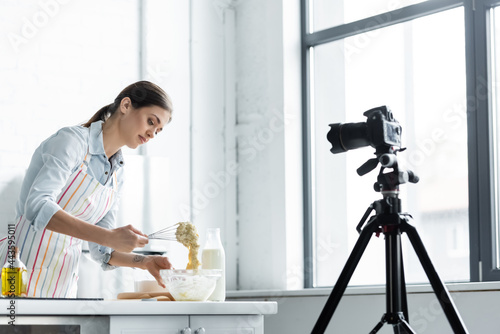 culinary blogger mixing dough in bowl in front of digital camera in kitchen. photo