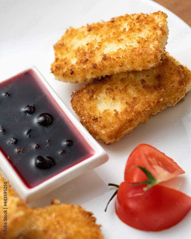 Pieces of cheese fried in breadcrumbs. Berry sauce and tomato on white plate. Close-up shot. Vertical format. Pieces of cheese fried in breadcrumbs. Berry sauce and tomato on white plate. Close-up shot. Vertical format.
