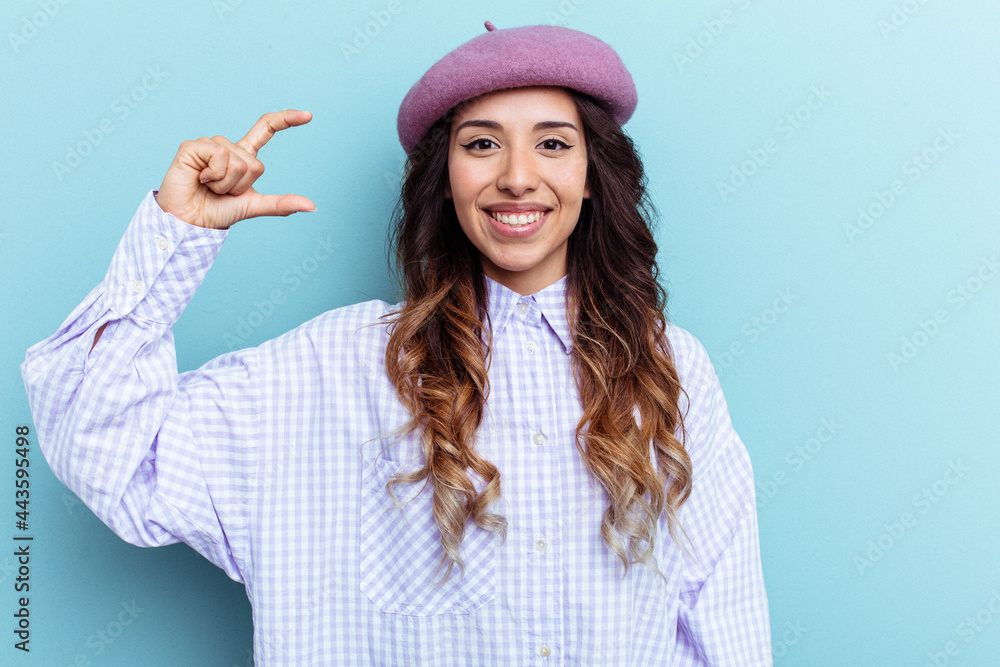 Young mexican woman isolated on blue background holding something little with forefingers, smiling and confident. Young mexican woman isolated on blue background holding something little with forefingers, smiling and confident.