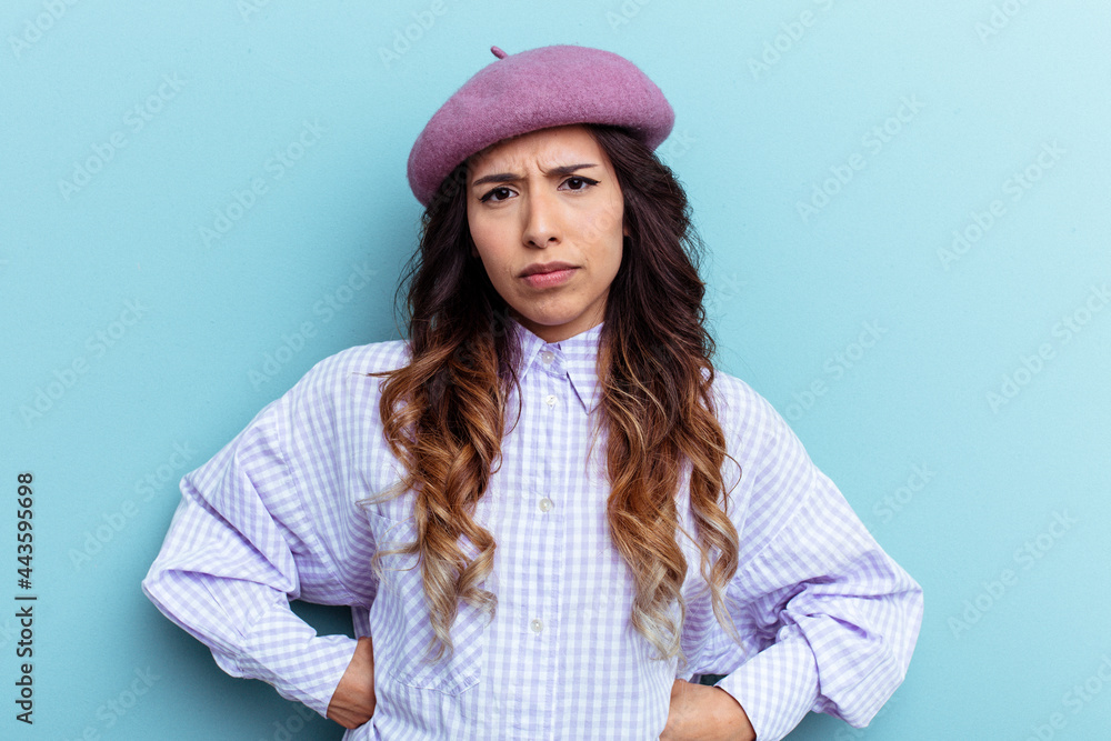 Young mexican woman isolated on blue background frowning face in displeasure, keeps arms folded. Young mexican woman isolated on blue background frowning face in displeasure, keeps arms folded.