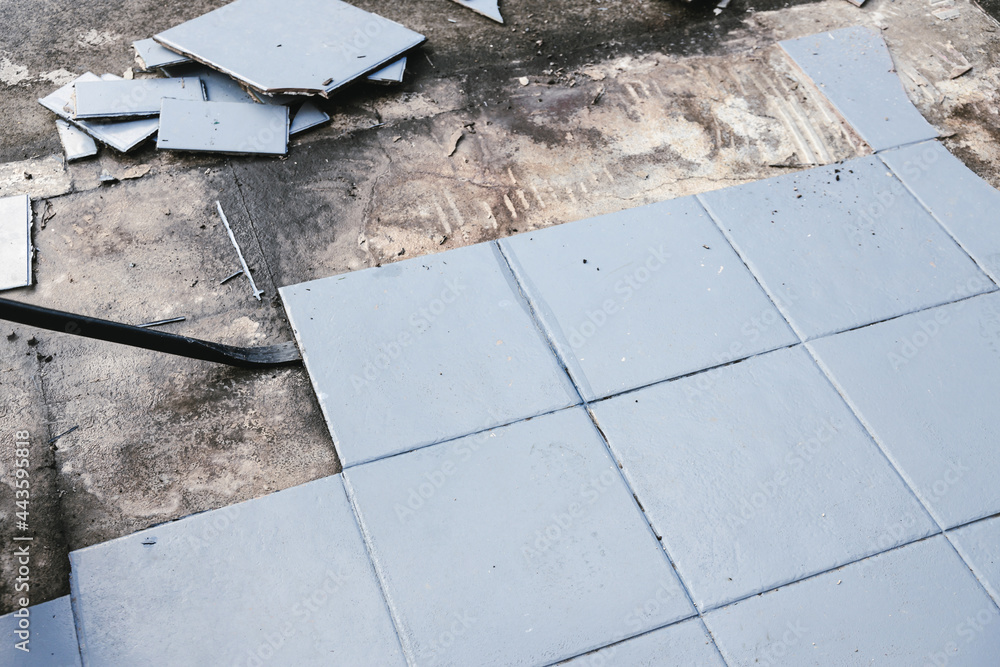 blue outdoor tiles getting ripped up to reveal concrete paving underneath, concept of demolition or renovation blue outdoor tiles getting ripped up to reveal concrete paving underneath, concept of demolition or renovation