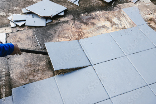 blue outdoor tiles getting ripped up to reveal concrete paving underneath, concept of demolition or renovation
