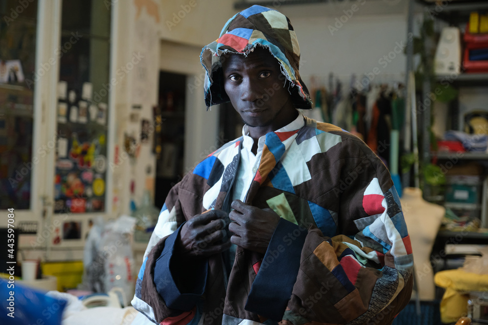 Portrait of an african man wearing traditional colorful clothes and hat at his sewing workshop.
