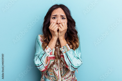 Young mexican woman isolated on blue background biting fingernails, nervous and very anxious.