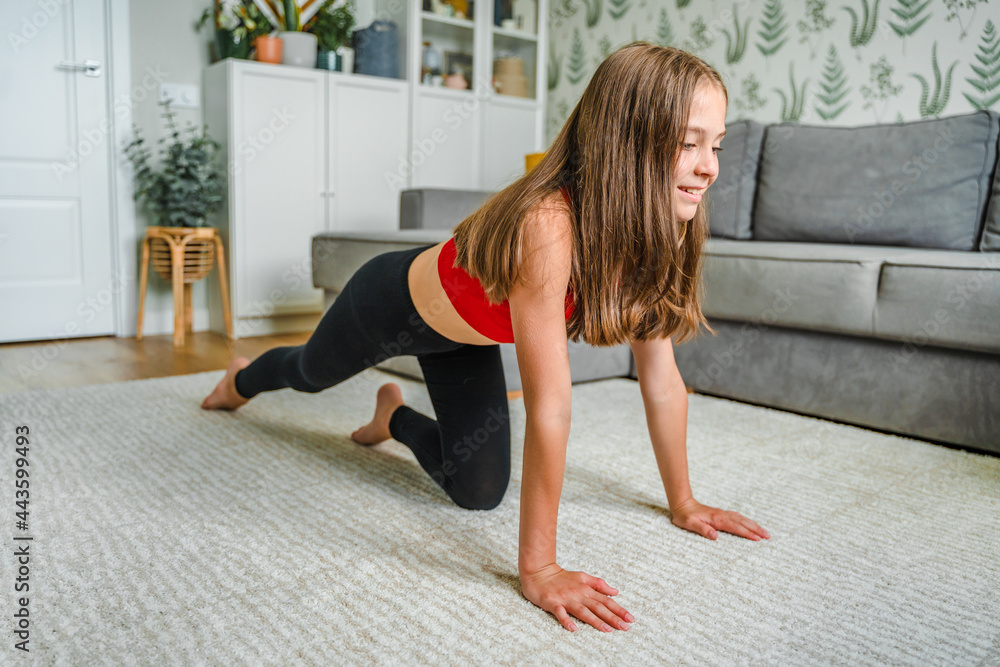 Obraz premium A cute little girl does yoga and trains stretching at home on a carpet in a modern living room interior