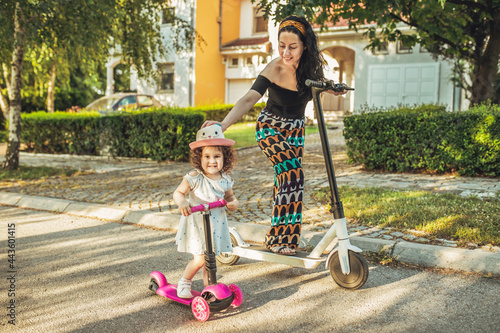 Mom and daughter ride scooters in their street.
