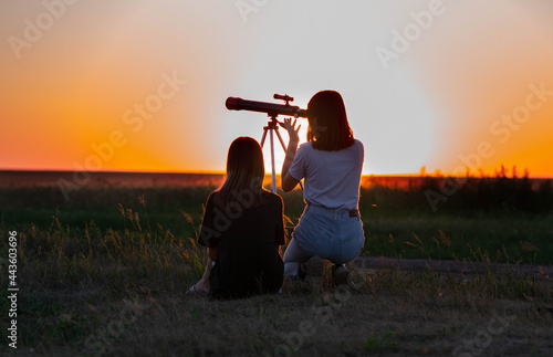 Girls at sunset in a field looking through a telescope