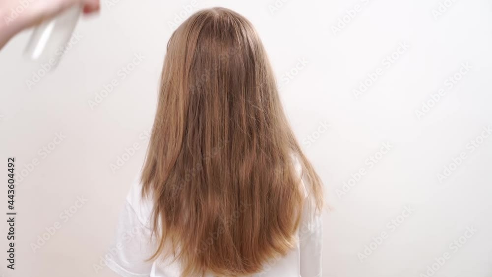 Mom applies a spray for easy combing on her daughter's hair. on a white background. care and cosmetics for children's hair. Mom applies a spray for easy combing on her daughter's hair. on a white background. care and cosmetics for children's hair.