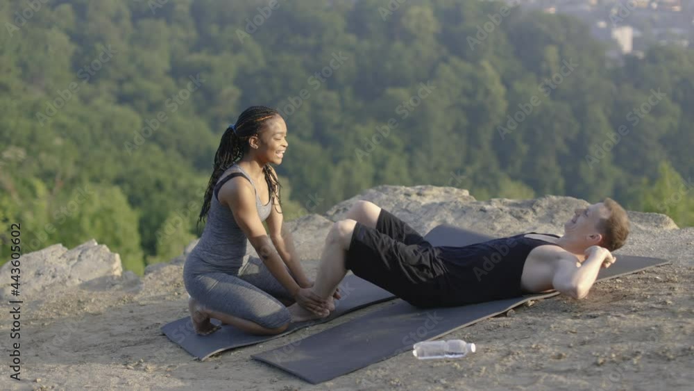Happy diverse couple in sport clothes giving high five while having workout for abs on top of hill. Cityscape on background. Active lifestyles. Happy diverse couple in sport clothes giving high five while having workout for abs on top of hill. Cityscape on background. Active lifestyles.